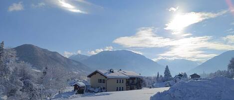 A snow-covered landscape with a house and mountains in the background.