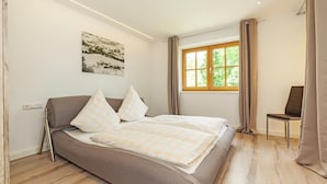 Ein Schlafzimmer mit einem Bett, einem Sessel, einem Fenster und einem Bild an der Wand.
