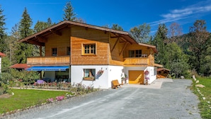 Ein zweistöckiges Holzhaus mit einem Balkon, einer Schotterauffahrt und einem Blumenblumenbeet.