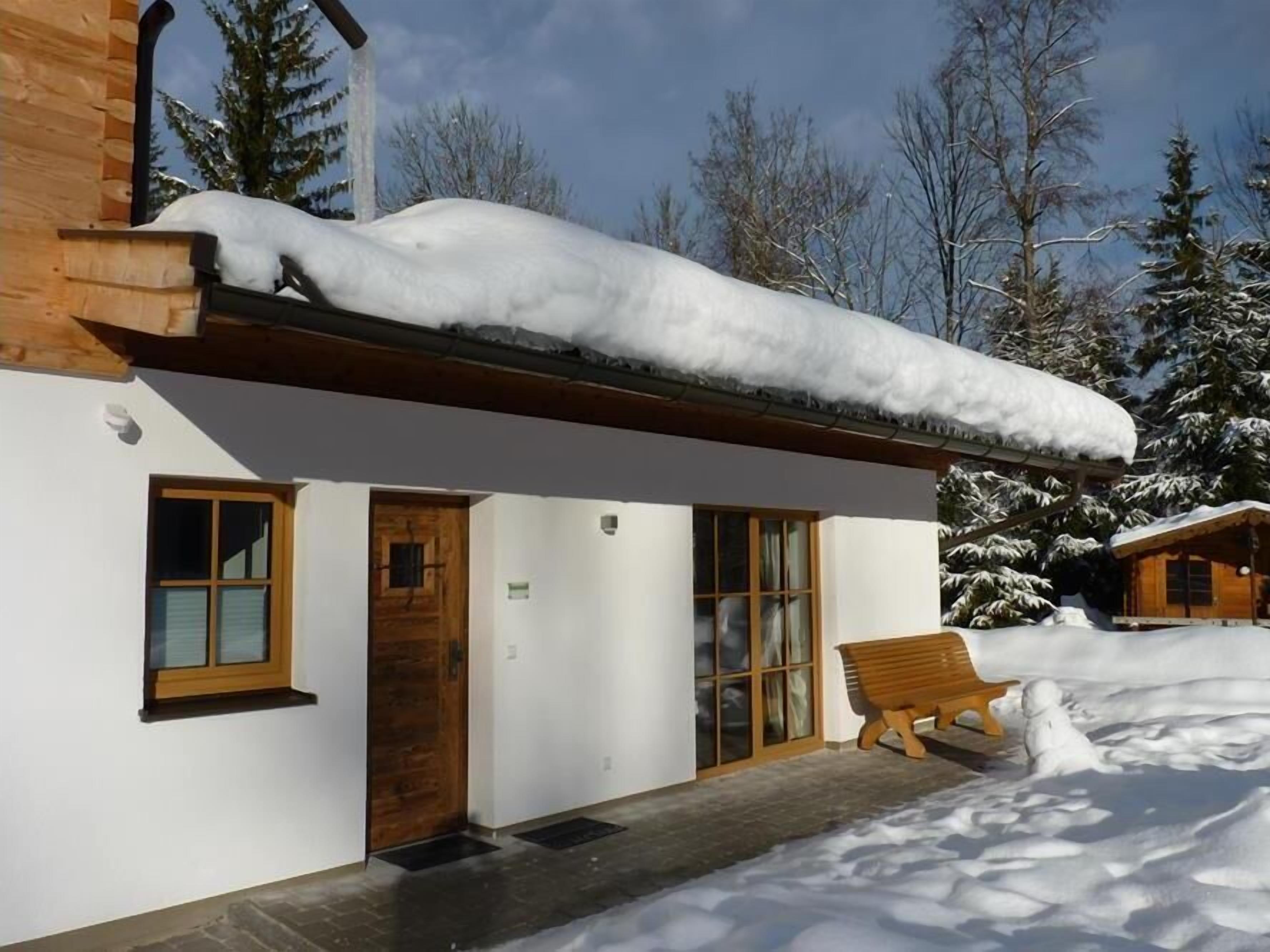 A snow-covered wooden cabin with a porch and a bench.
