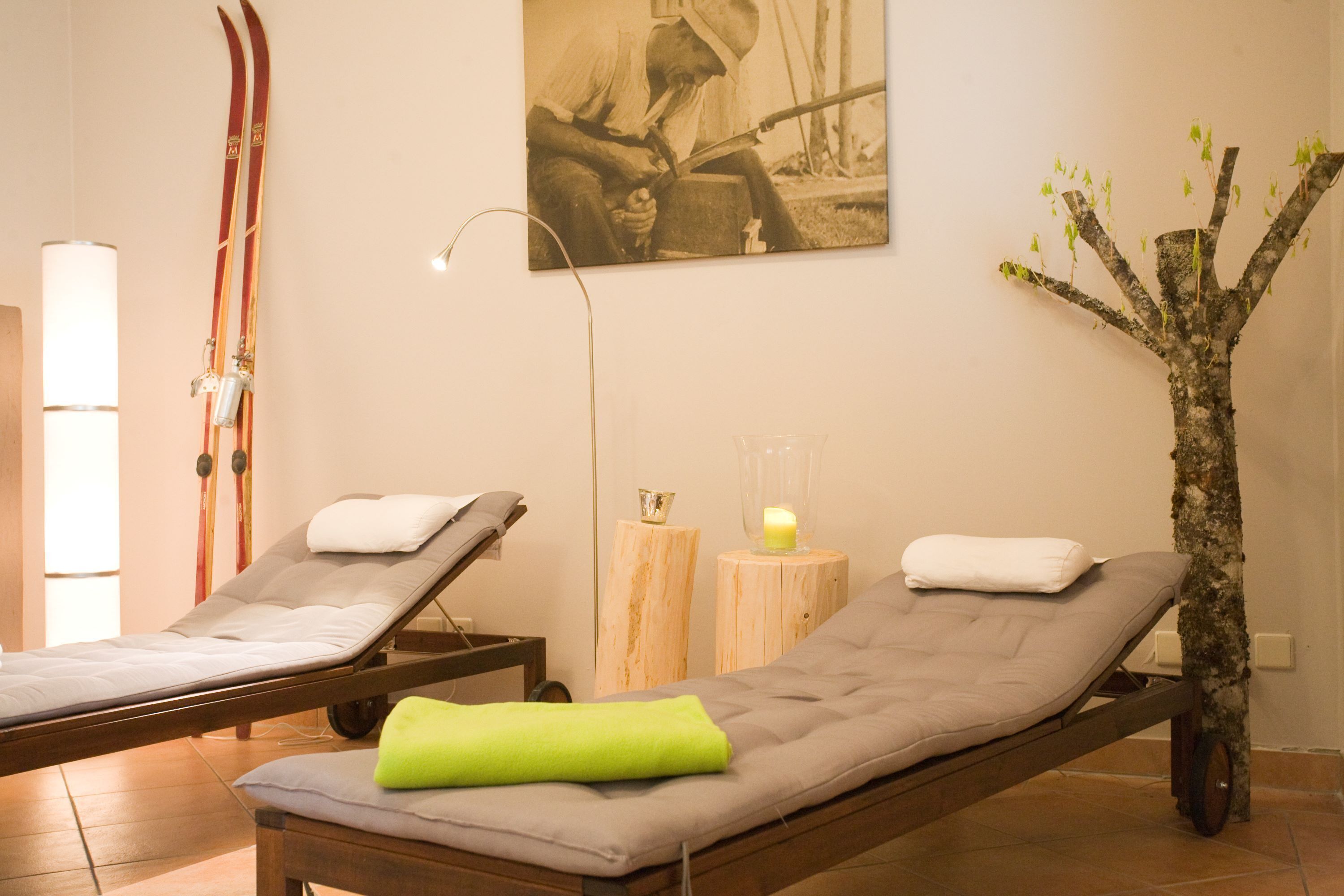 A spa room with two massage tables, a wooden tree sculpture, and a wall-mounted picture.