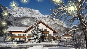 A snow-covered mountain lodge with a wooden exterior, multiple balconies, and a large tree in front. - Ferienwohnung Dahoam für 2-6 Personen, 78 qm (Marktschellenberg)