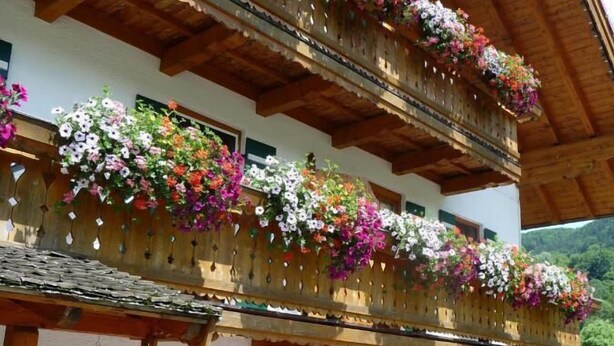 A traditional chalet with wooden balconies adorned with colorful flowers, a wooden door, and a sign indicating a restaurant. - Ferienwohnung Dahoam für 2-6 Personen, 78 qm (Marktschellenberg)
