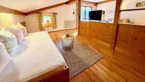 Ein Zimmer mit einem Bett, einem kleinen runden Tisch, einem Fernseher und einem Fenster mit Vorhängen.
