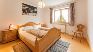A bedroom with a wooden bed, bedside tables, a nightstand, a window with curtains, and a wall-mounted picture. - Ferienwohnung I° extra Schlafzimmer, Süd-Terrasse, 65 qm° (Aschau im Chiemgau)
