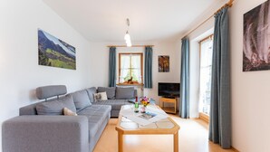 A modern living room with a grey sofa, a wooden coffee table, and a television on a stand. - Ferienwohnung I° extra Schlafzimmer, Süd-Terrasse, 65 qm° (Aschau im Chiemgau)