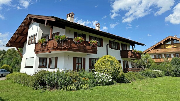 A two-story building with a balcony, a chimney, and a garden in front. - Ferienwohnung I° extra Schlafzimmer, Süd-Terrasse, 65 qm° (Aschau im Chiemgau)
