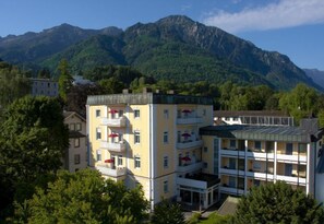 Een meerhoog hotel met balkons, omgeven door weelderige begroeiing en bergen op de achtergrond.