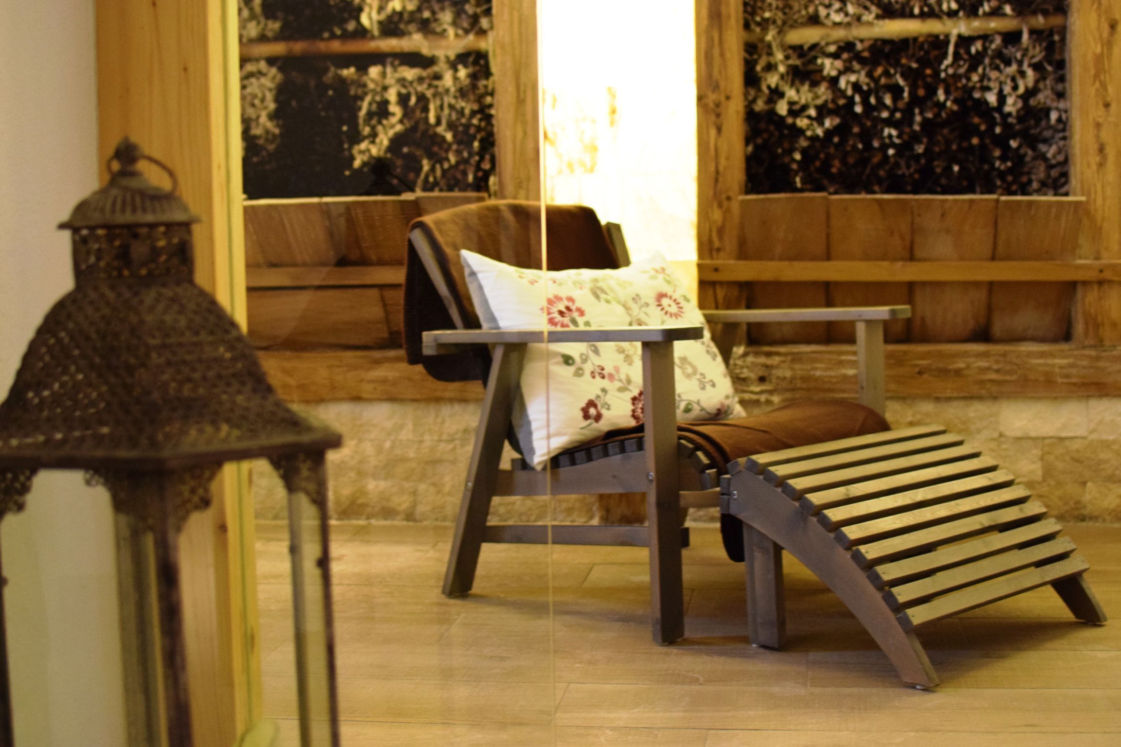 A wooden bench with a cushion, a small table, and a lantern in a room with wooden walls and a window.