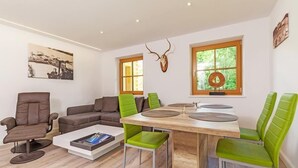 A modern living room with a wooden dining table, green and brown leather sofas, and a mounted deer head on the wall. - Ferienwohnung van Hees, "Benz Eck" (Reit im Winkl)