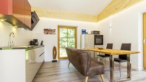 A modern kitchen with a wooden ceiling, a dining area with a brown leather chair, and a view of greenery through a large window. - Ferienwohnung van Hees, "Benz Eck" (Reit im Winkl)