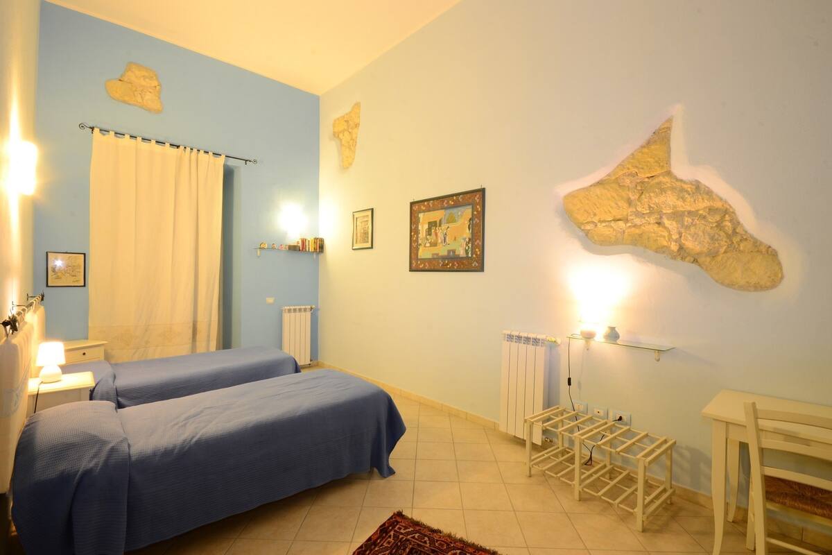 A bedroom with two beds, a radiator, a shelf with books, and a map on the wall.
