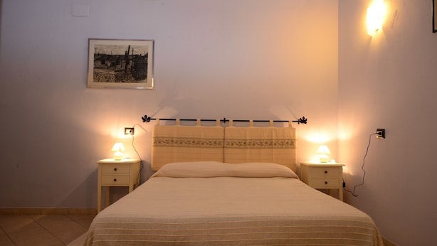A bedroom with a bed, two bedside tables, a wall-mounted light, and a framed picture. - B&B Su Niu (Cagliari)