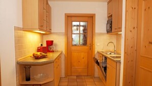Une cuisine compacte avec des meubles en bois, un pare-feu en carrelage, un évier et une fenêtre en verre dépoli.