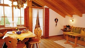 Une pièce chaleureuse avec une table à manger en bois, mise pour le petit-déjeuner, un canapé et un lustre.