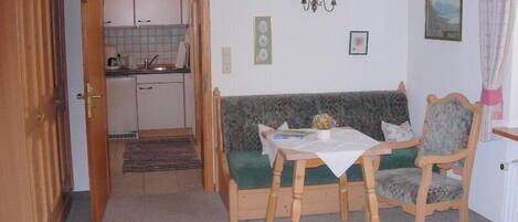 Une pièce chaleureuse avec un banc en bois, une petite table et, au fond, une cuisine.