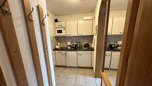 A narrow kitchen with white cabinets, a microwave, and a coffee maker. - 2-Raum-Ferienwohnung, 47m², Dusche/WC, Balkon und Küche extra (Reit im Winkl)