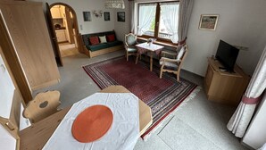 A compact living space with a sofa, a dining table, a TV, and a patterned rug. - 2-Raum-Ferienwohnung, 47m², Dusche/WC, Balkon und Küche extra (Reit im Winkl)