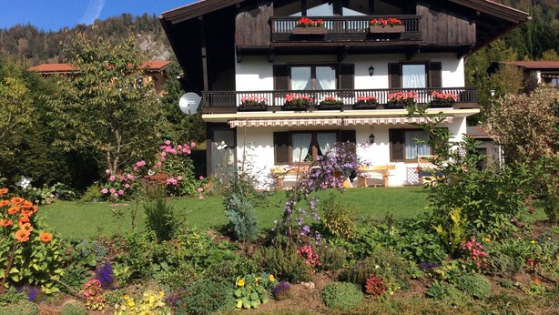 A two-story chalet with balconies, surrounded by a well-maintained garden with various flowers and shrubs. - 2-Raum-Ferienwohnung, 47m², Dusche/WC, Balkon und Küche extra (Reit im Winkl)