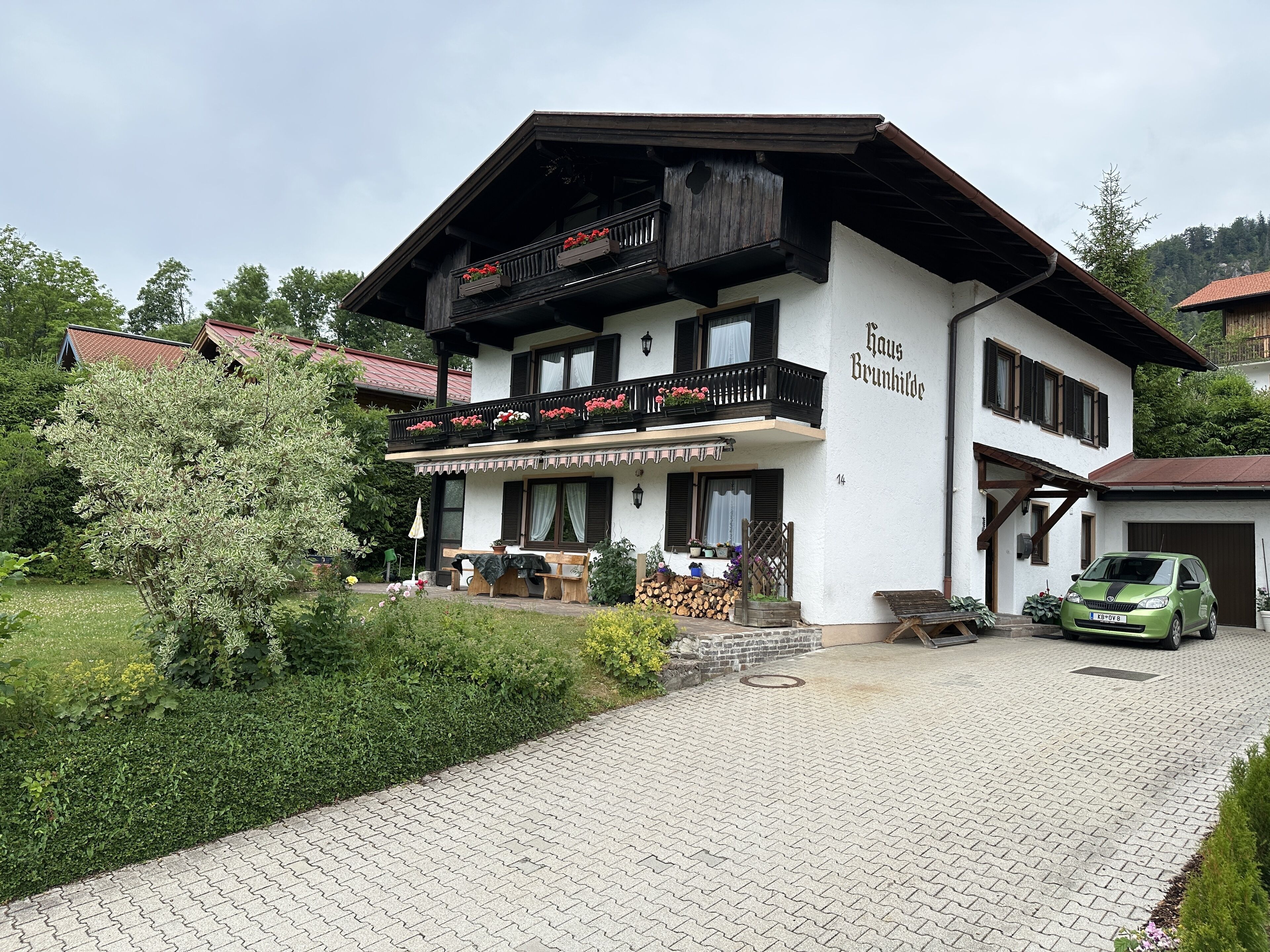 Ein zweistöckiges Gebäude mit einem Balkon und einer gepflasterten Auffahrt. Auf dem Schild steht "Haus Brunnhilde".