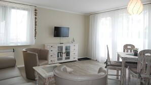 Een woonkamer met een bank, salontafel, televisie, kast en een eethoek met stoelen en een tafel.
