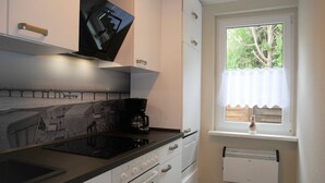 Een moderne keuken met een zwart fornuis, witte kasten en een raam met uitzicht op groen.