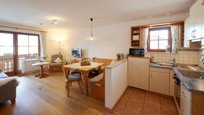 Une cuisine compacte avec un coin repas, des meubles en bois, un téléviseur et une fenêtre avec des rideaux.