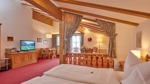 Et hotelværelse med seng, trægavl, fjernsyn, skrivebord med stol og et vindue med gardiner.