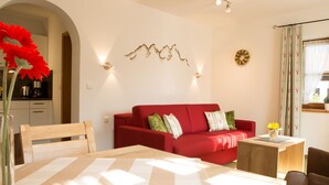 Una sala de estar con un sofá rojo, una mesa de comedor de madera y una cocina al fondo.