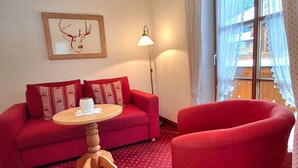 Un canapé rouge avec des coussins à motifs, une table basse en bois et un fauteuil rouge dans une pièce dont le tapis est à pois.