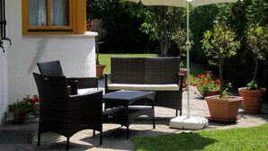 Une terrasse extérieure avec des meubles en osier, un parasol blanc et des plantes en pot.