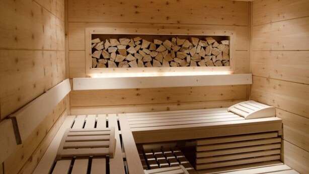 Un sauna avec des murs et des bancs en bois, un foyer avec des bûches et un banc doté d’un dossier.