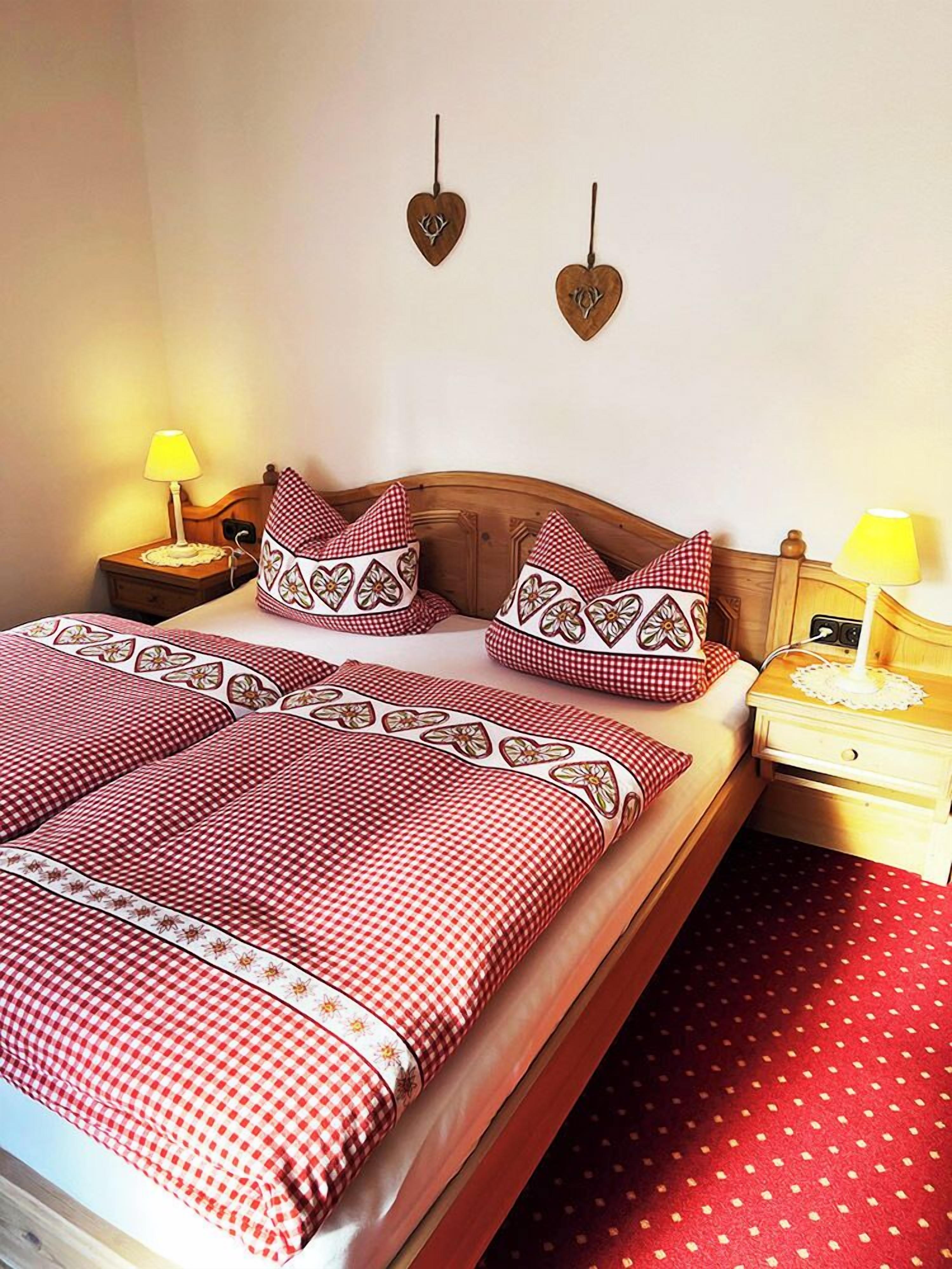A neatly made bed with checkered bedding, two heart-shaped wall decorations, and two bedside lamps.