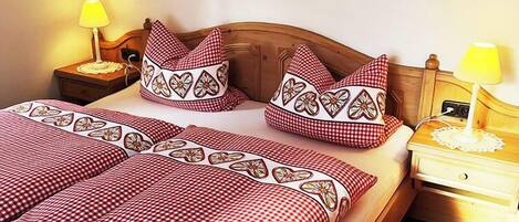 A neatly made bed with checkered bedding, two heart-shaped wall decorations, and two bedside lamps.