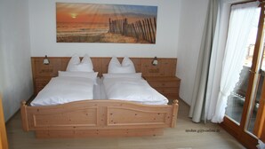 A double bed with white linens, wooden headboard, two bedside tables, and a painting of a sunset over a beach. - (2) Ferienwohnung 36m², 2 Personen mit seperaten Schlafzimmer, Du/WC, Balkon (Reit im Winkl)