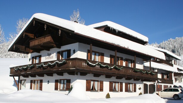 A multi-story chalet with a snow-covered roof, wooden balconies, and a sign indicating it is a 'Haus Sonnenbichl'. - (2) Ferienwohnung 36m², 2 Personen mit seperaten Schlafzimmer, Du/WC, Balkon (Reit im Winkl)