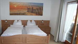 A double bed with white linens, wooden headboard, two bedside tables, and a painting of a sunset over a beach.