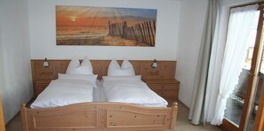 A double bed with white linens, wooden headboard, two bedside tables, and a painting of a sunset over a beach.