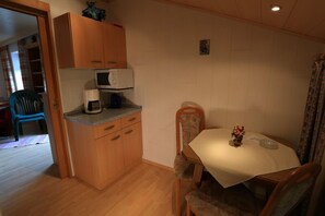 Una cocina compacta con armarios de madera, microondas y una mesa de comedor con sillas.