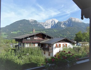 A chalet with a balcony, surrounded by lush greenery and mountains in the background.