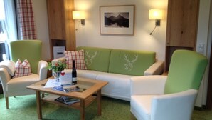 A cozy living room with a green sofa, white armchairs, a wooden coffee table, and a framed picture on the wall. - Ferienwohnung Nr. 2 Kehlsteinblick, 1 bis 2 Personen, 45 qm, 1 Schlafzimmer, Wohnküche und Balkon (Schönau am Königssee)