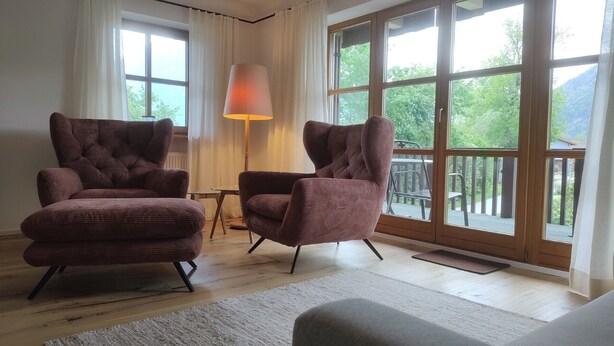 Una habitación con dos sillones amplios, una mesita, una lámpara y ventanas grandes con vistas a zonas verdes.