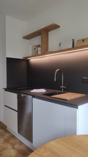 Una cocina moderna con lavavajillas de acero inoxidable, encimera negra, estante de madera y pileta con grifo integrado.