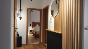 Un pasillo que conduce a un dormitorio con una cama, un armario de madera, un espejo y una lámpara.