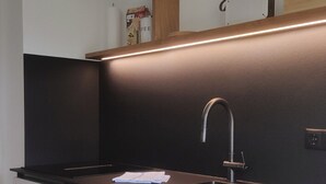 Una cocina moderna con lavavajillas de acero inoxidable, encimera negra, estante de madera y pileta integrada.