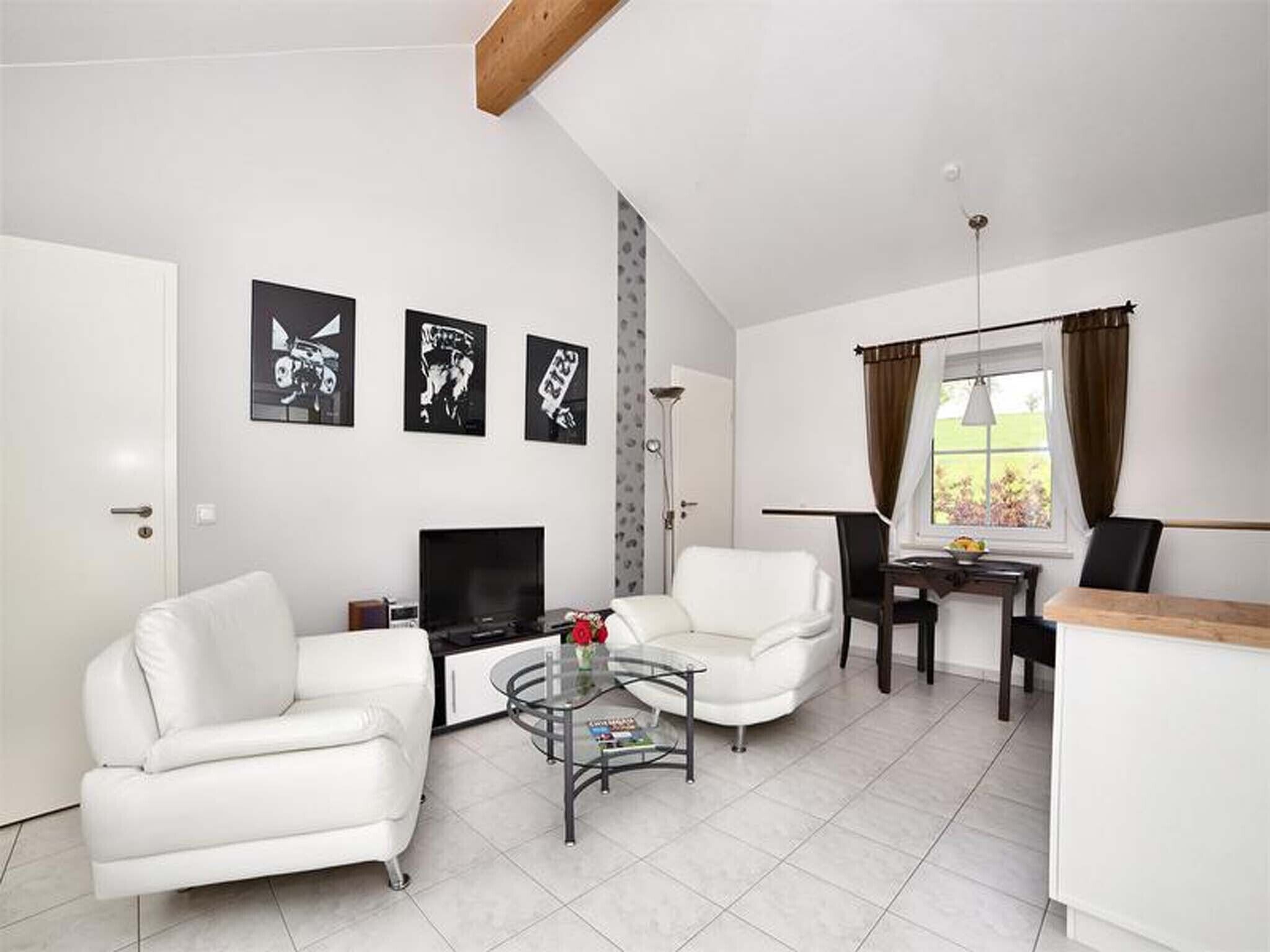 Una sala de estar moderna con un sofá, un sillón, un televisor y una mesita de centro. Hay tres cuadros en blanco y negro colgados en la pared.
