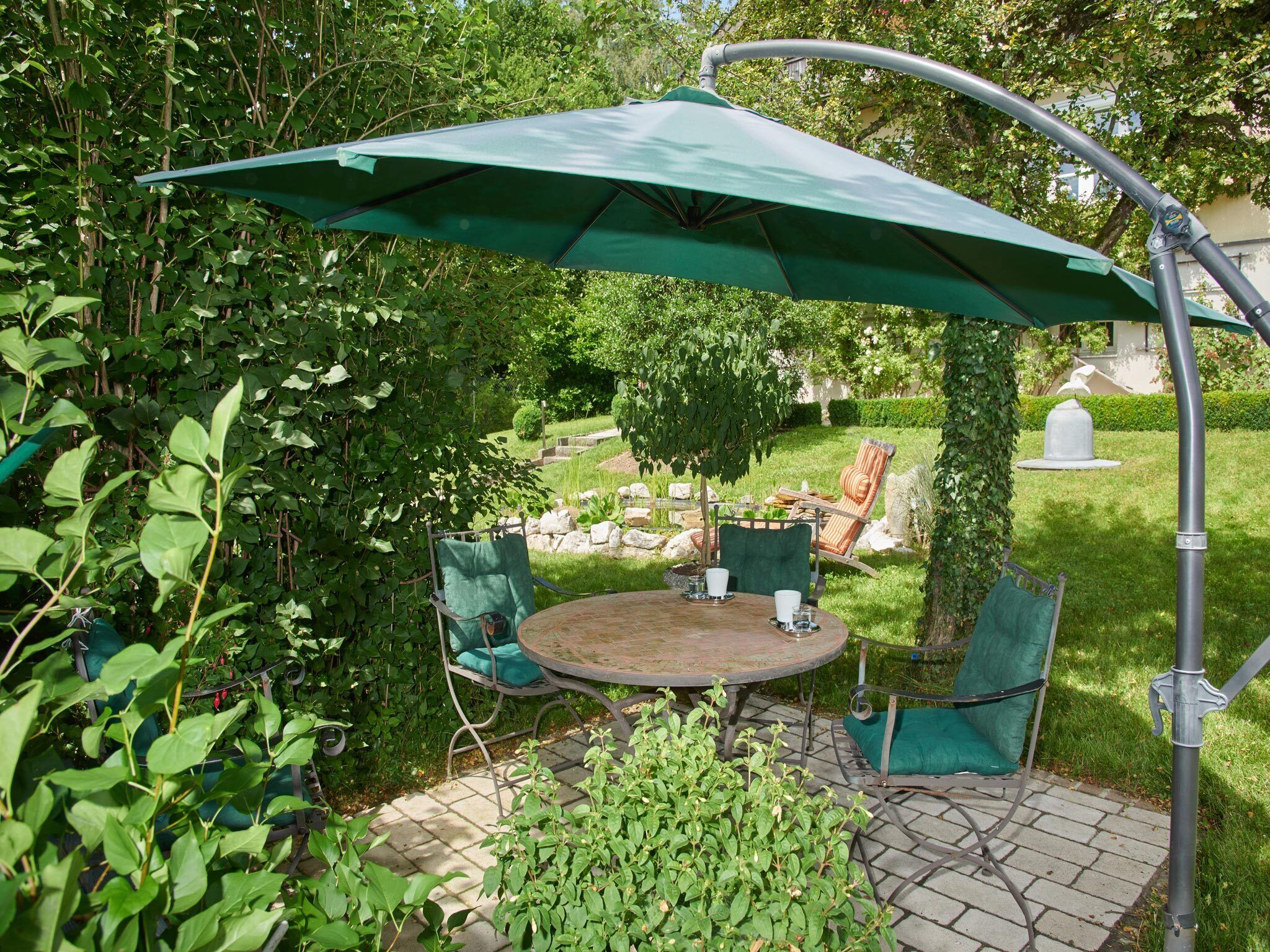 A patio with a round table and chairs, a green umbrella, and a garden setting.