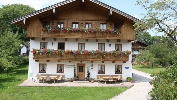 Un bâtiment traditionnel en bois, doté d’un balcon orné de fleurs, d’une enseigne indiquant « Zuchterhaus » et d’un espace extérieur aménagé pour s’asseoir.