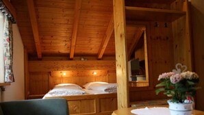 A wooden cabin room with a bed, a small table, and a window with curtains.