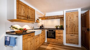 A modern kitchen with wooden cabinetry, a black countertop, and a built-in oven. - Ferienwohnung "Beim Sepperl" im Zuhäusl, 1-2 Personen, 40 qm, Dusche/WC, Südbalkon, TV, 1 Schlafzimmer,Nichtraucher (Ramsau bei Berchtesgaden)